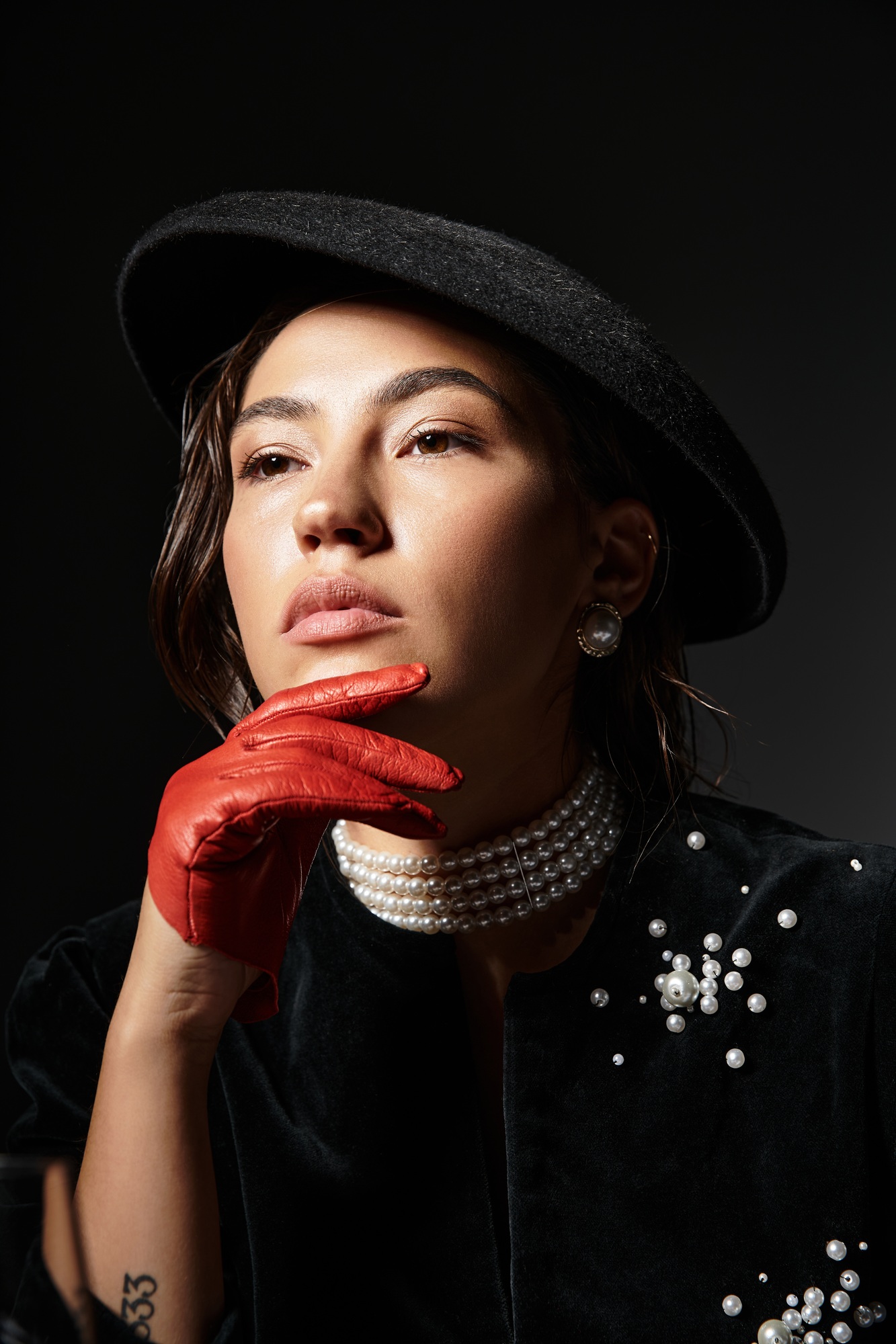 Sophisticated young woman in elegant attire poses thoughtfully against a contrasting dark background